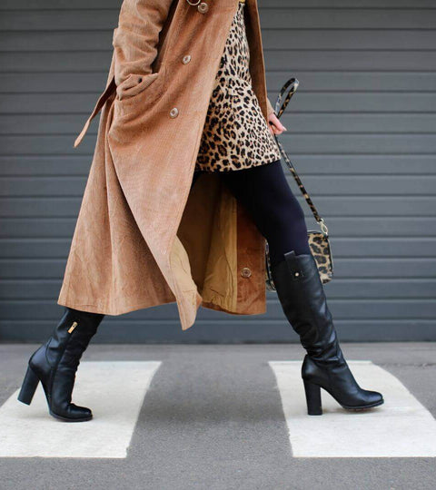 Woman in a trench coat and high boots walking confidently down the catwalk during a fashion show.