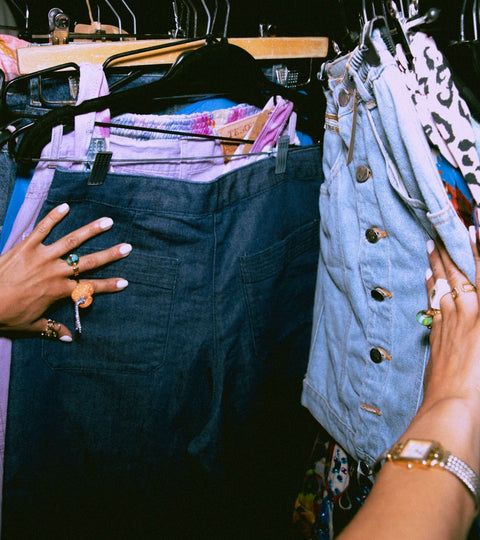 Hands browsing rails of second-hand denim and fast fashion garments — highlighting resale culture.