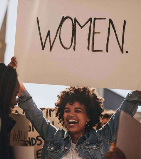 woman holding up a sign saying WOMEN in demo on women rights