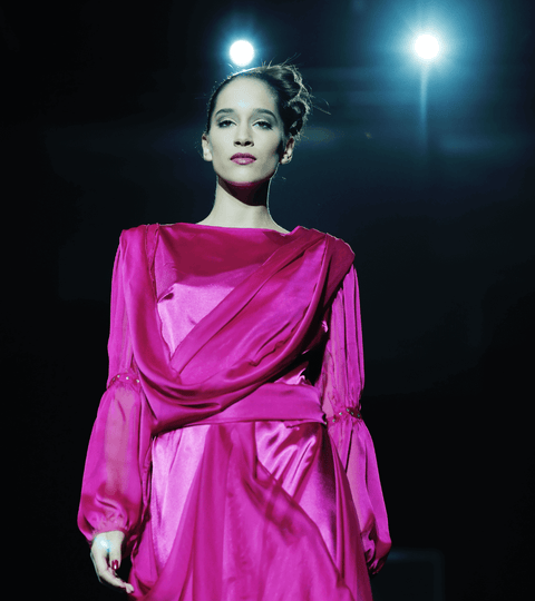 Model walking London Fashion Week runway in bright pink satin dress under spotlights
