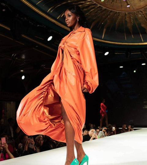 Model walking down a catwalk in an orange dress illustrating the trickle movement in fashion