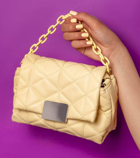A stylish yellow quilted handbag showcased against a vibrant purple background, highlighting 2024 fashion trends recap.