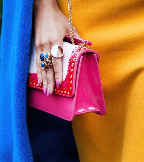 Close-up of hand holding a pink handbag with gold chain strap, styled with blue coat and yellow dress