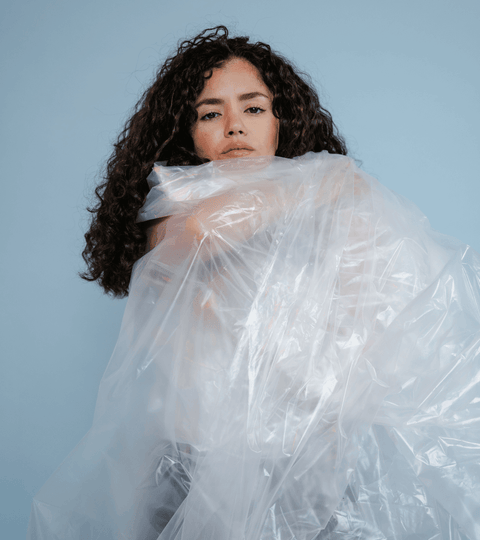 Polyester pollution represented by a model surrounded by plastic material highlighting fashion's synthetic fibre crisis