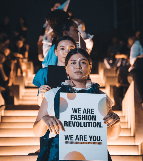 Models on a catwalk holding protest signs calling for fashion industry accountability