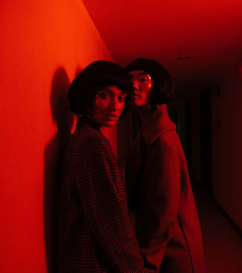 Two models in sleek outfits illuminated by red light, showcasing haute couture SS22 style in an artistic hallway.