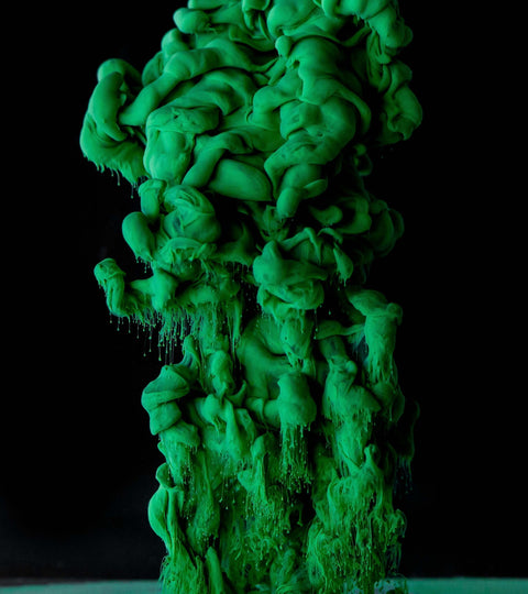 Vibrant green paint swirling and forming cloud-like shapes against a black background.