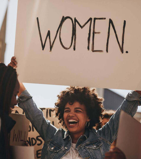 woman holding up a sign saying WOMEN in demo on women rights