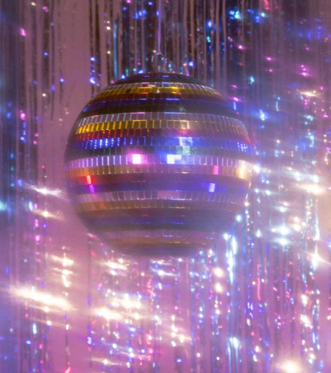 Disco ball reflecting colorful lights surrounded by shiny decorations, symbolizing celebration and pride in fashion.