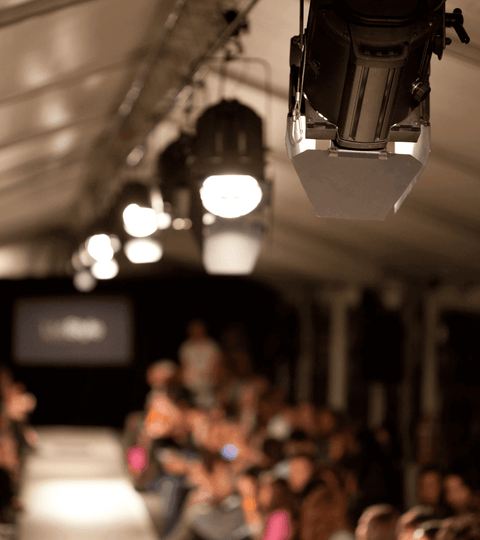 Reviewing Inside Vogue: Inventing the Runway Exhibition with fashion runway lights and audience in background.